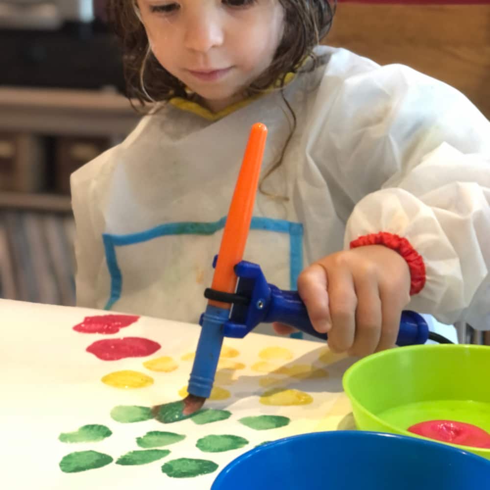 Xanthe using the FUNctionalHand to hold a paint brush. She is creating different colours spots.