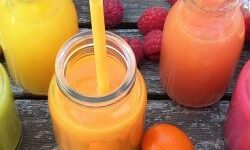 Colourful smoothies with straws in a row surrounded by fruit