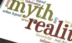 Myths and reality written in green and red on a tablet lying on a table next to a white cup of coffee and a stylus. There are other words around myth and reality, including logic, fiction, information, proof and false